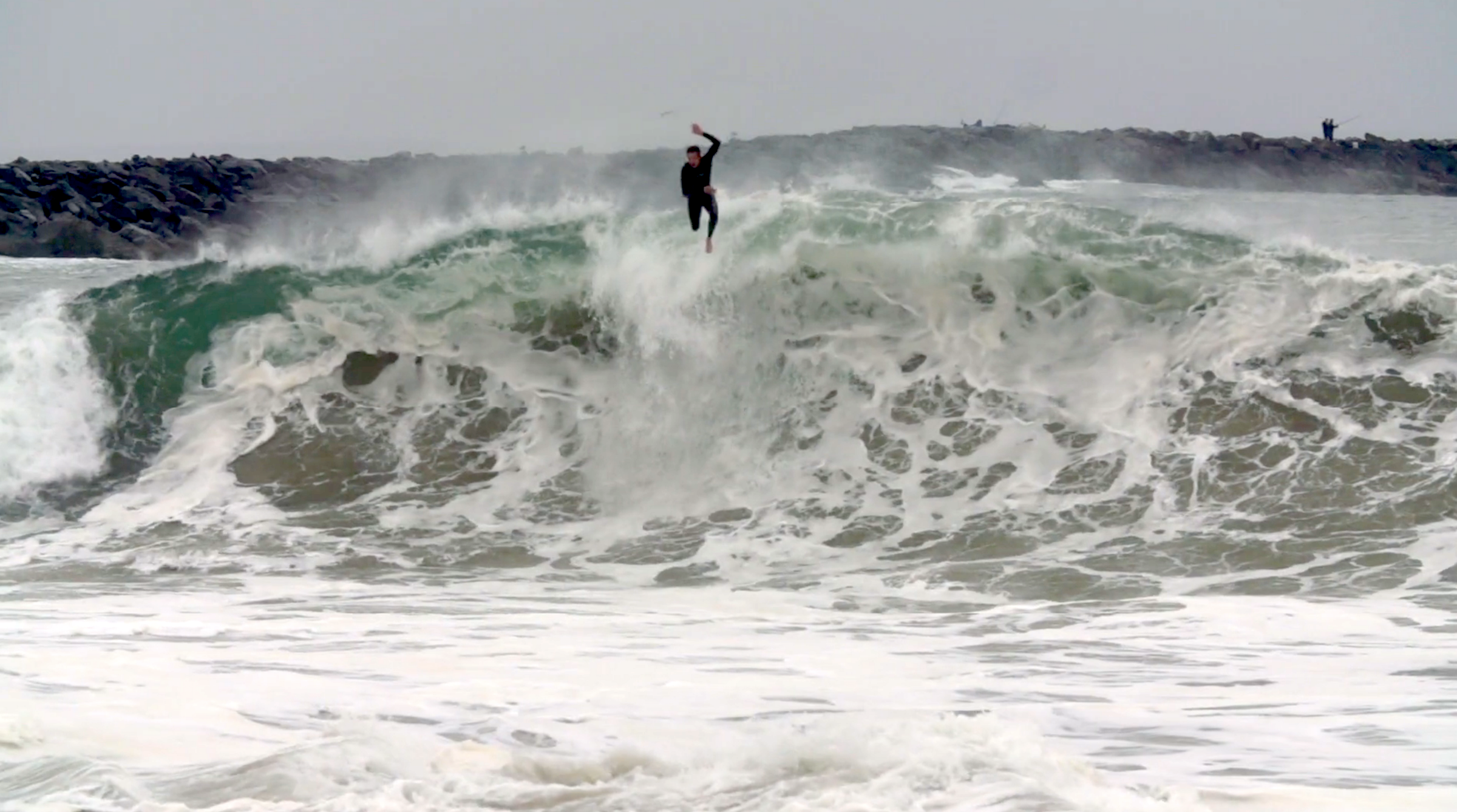 man in black wetsuit body surfing and leaping from frothy wave