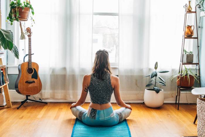 woman sitting cross legged on hemp yoga mat facing window