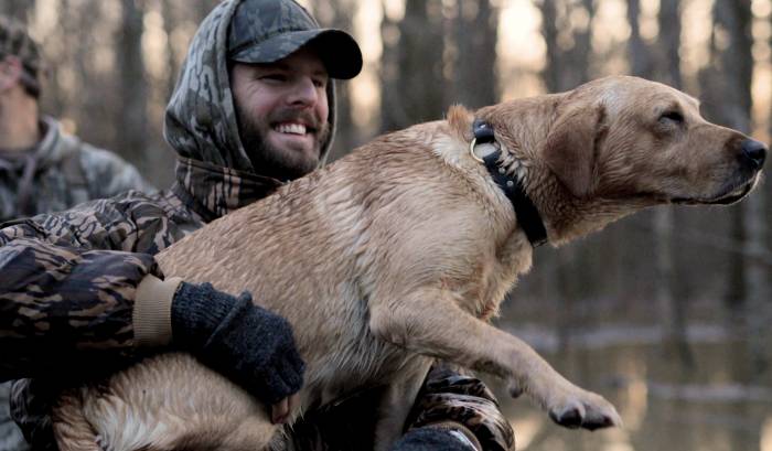 man smiling holding his waterfowl hunting dog in arms