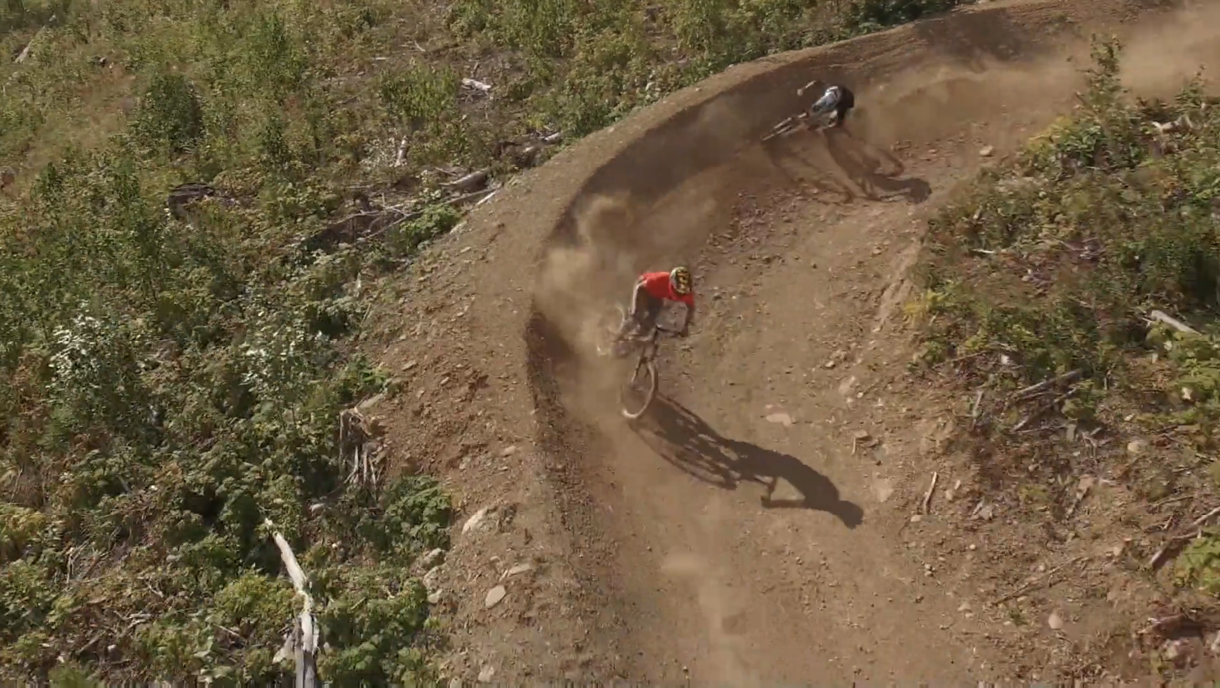 two people biking fast across dirt berm in Revelstoke BC