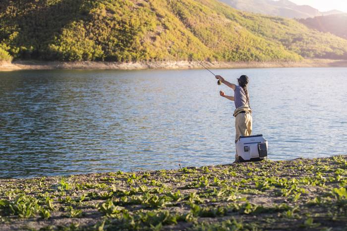 female angler on shore of lake with OtterBox trooper cooler