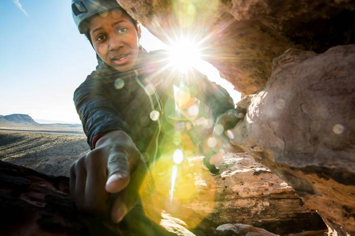 Woman rock climbing sun at back