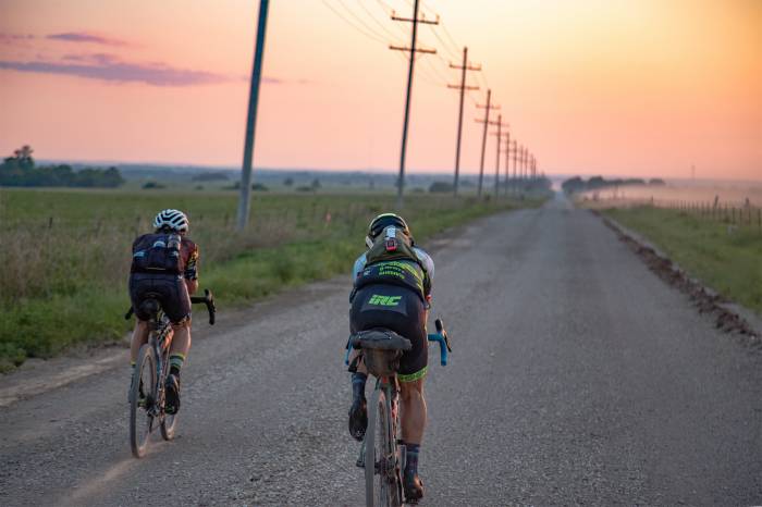 two cyclists riding into a sunset along a gravel road