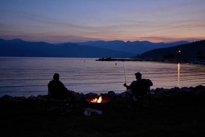 Two people sitting by campfire and lake