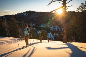 people skinning uphill at dusk with the yellow sun behind them