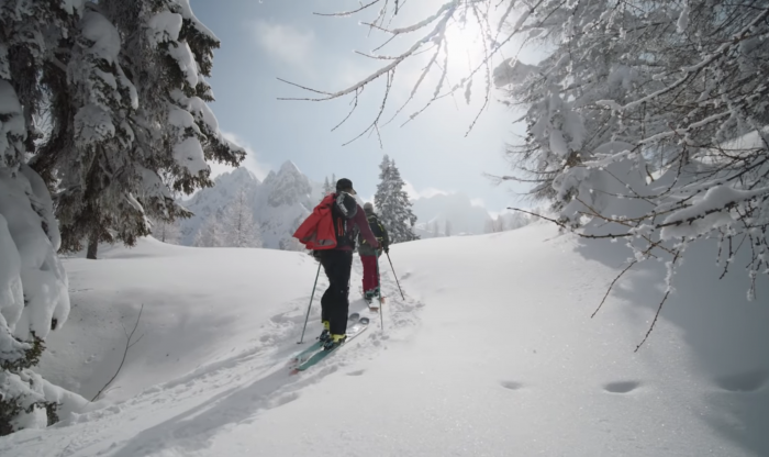 elyse saugstad skinning uphill using poles and wearing red backpack