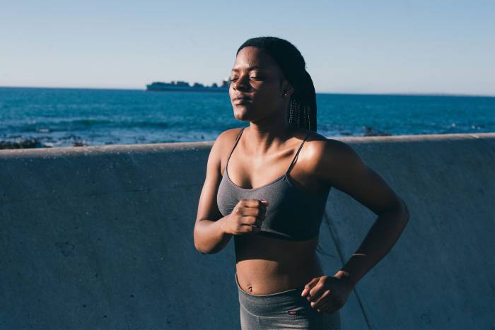 Black woman running with eyes closed along coast in sports bra and tights