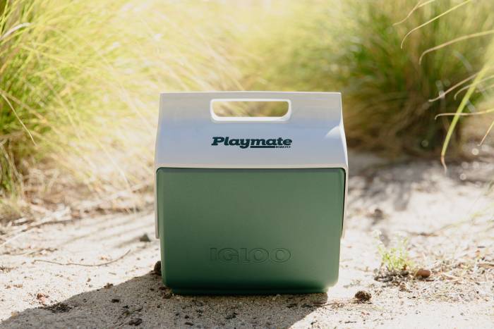 A green Igloo Playmate cooler resting on sandy trail in sunshine