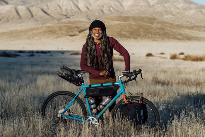 The Bicycle Nomad Erick Cedeño in field with teal blue framed bike