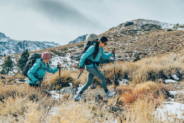 Two female hikers in matching jackets hiking uphill in winter