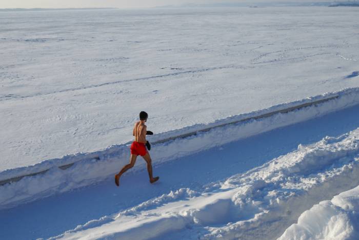 man running in red shorts barefoot down lane of snow