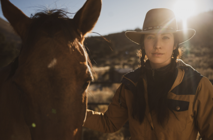 gillian larson in cowboy hat standing next to her horse on a trail