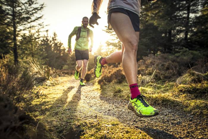 two runners running down trail with sun setting in background