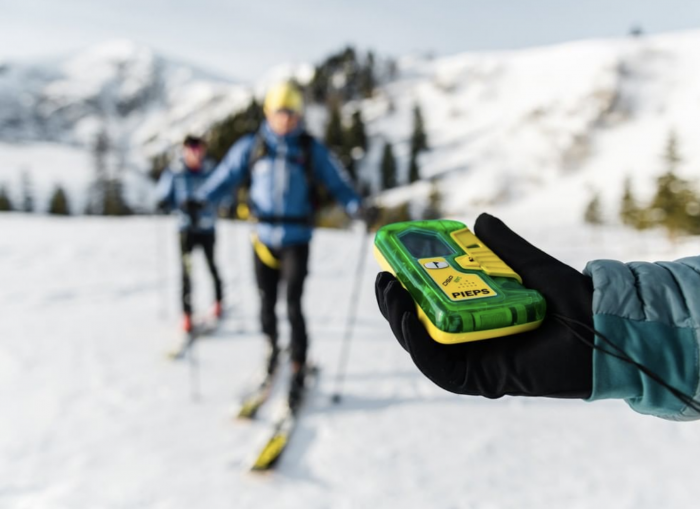 skier holding up pieps dsp pro transceiver with two other skiers in background