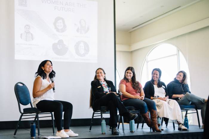 5 women, one holding a microphone, on a speaking panel at a Women's Outdoor Summit