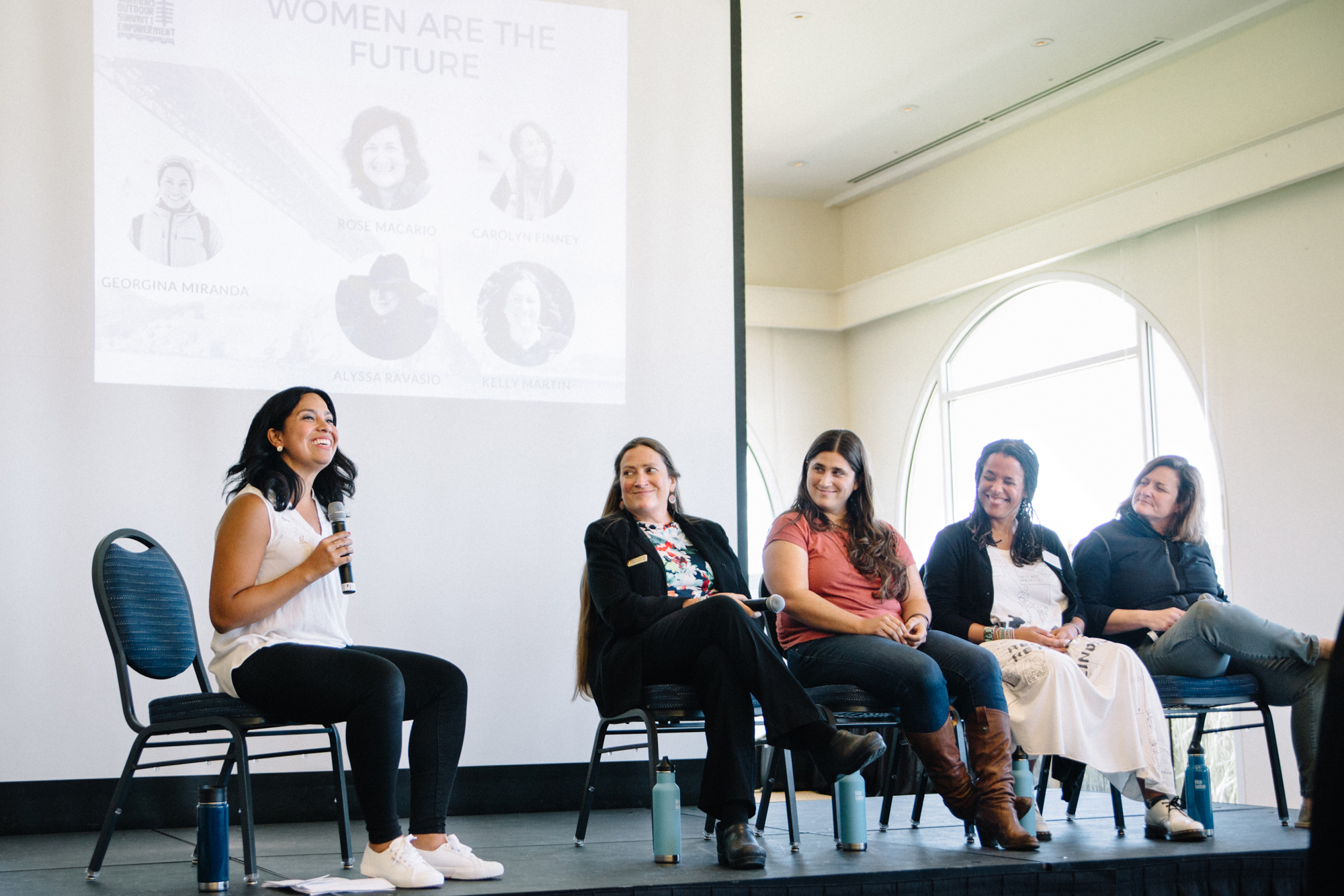 5 women, one holding a microphone, on a speaking panel at a Women's Outdoor Summit
