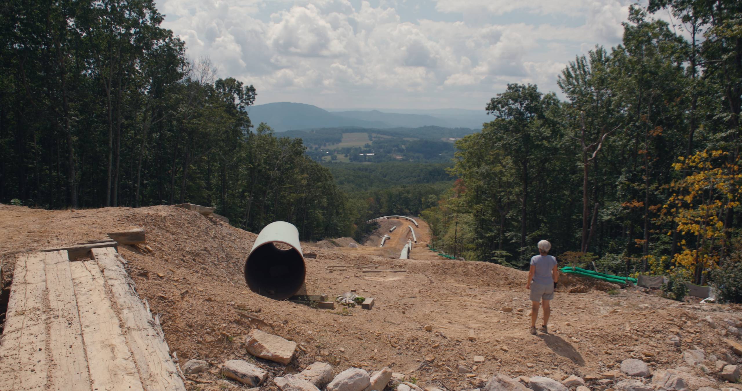 a person looking down a steep hill cluttered with segments of a pipeline