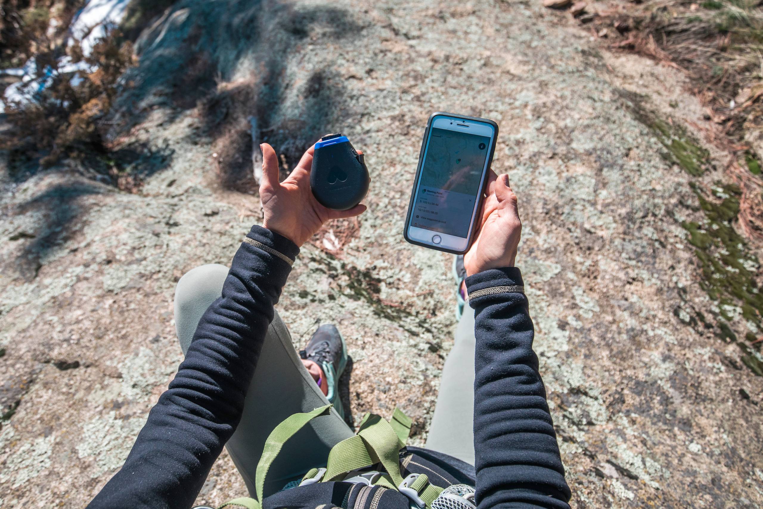 Somewear Labs and onX waypoints satellite app hiker holding a Somewear hotspot and smartphone while sitting on a rock