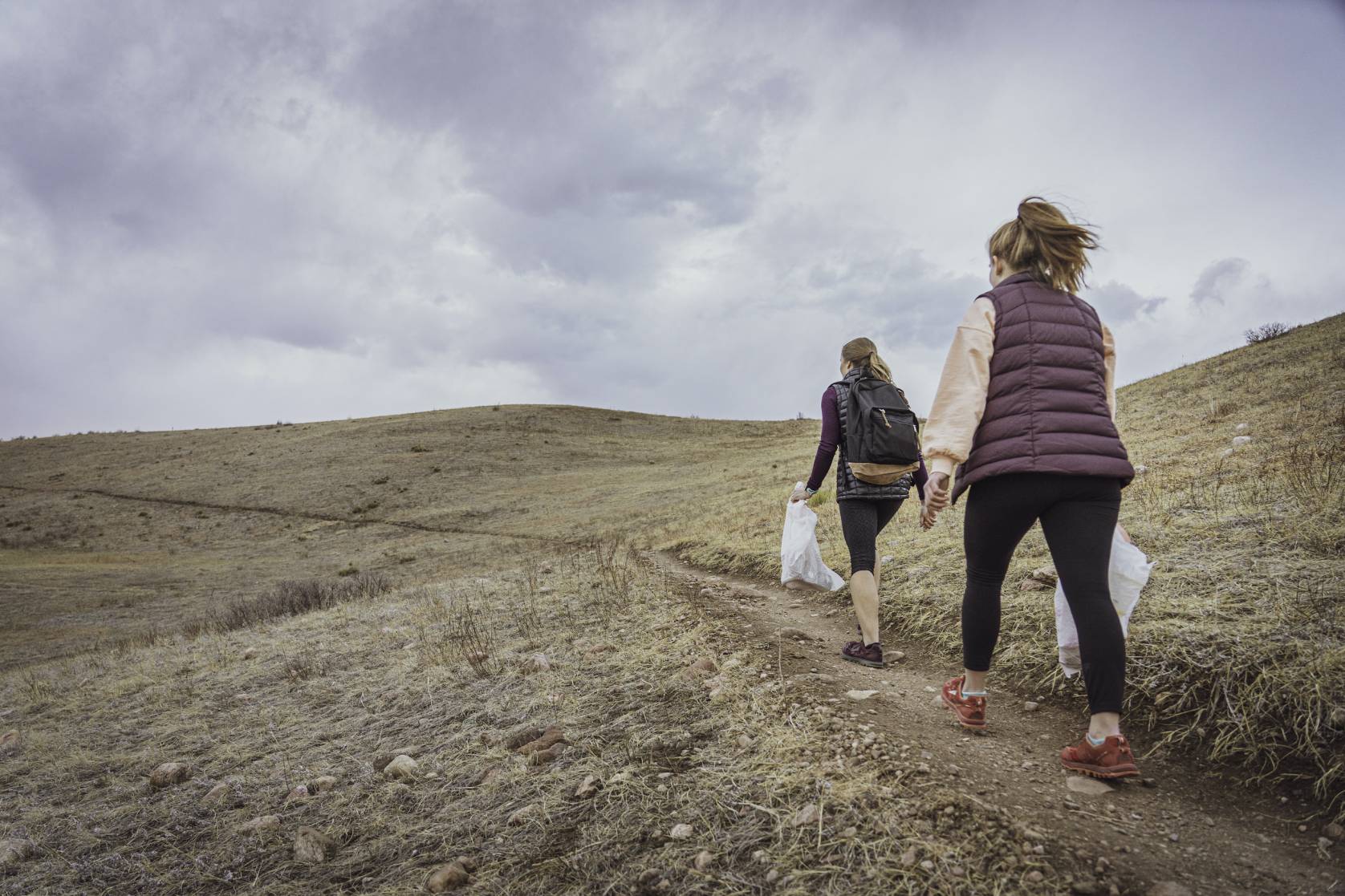 two female hikers with trash bags walking uphill