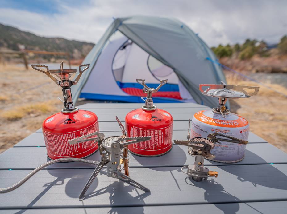 The Best Backpacking Stoves of 2021 five different lightweight backpacking stoves with fuel canisters and a tent in the background
