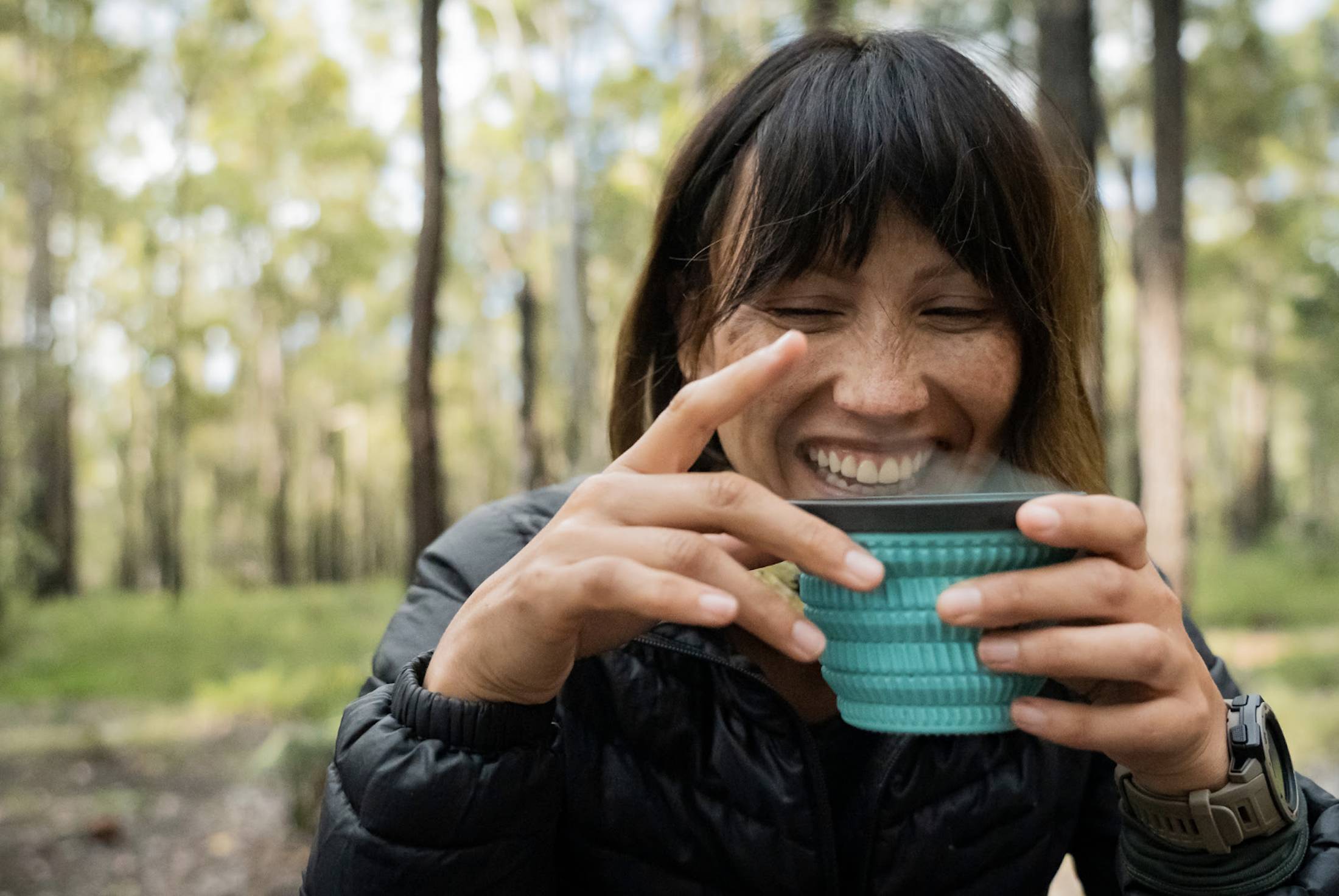 woman smiling and drinking from a teal sea to summit cool grip mug