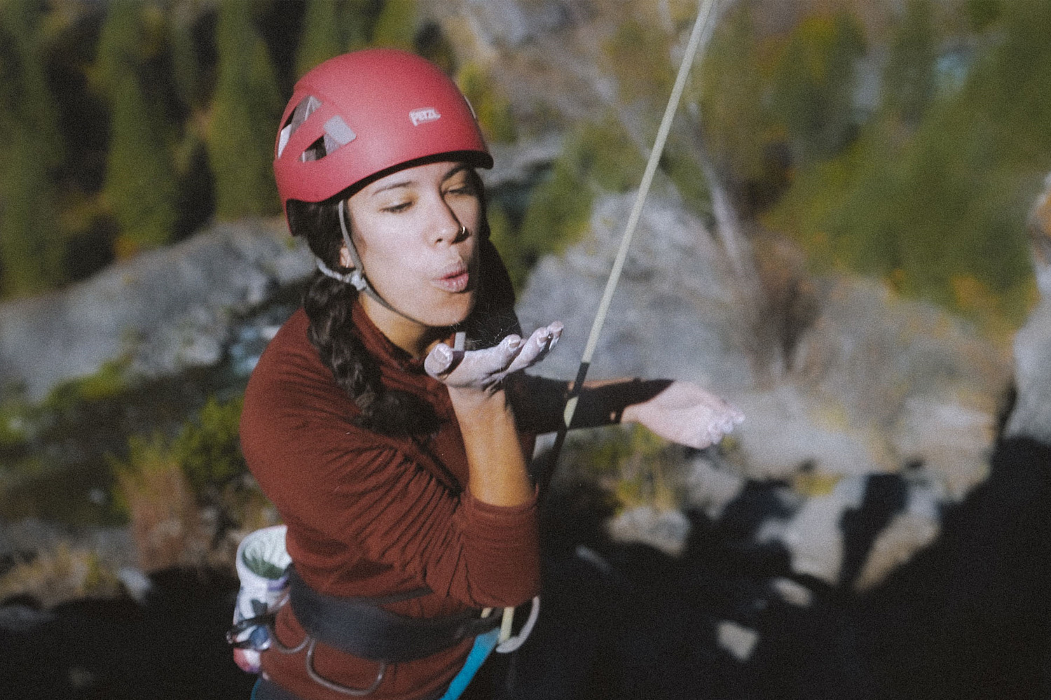 female climber of color roped in blowing chalk off her hand