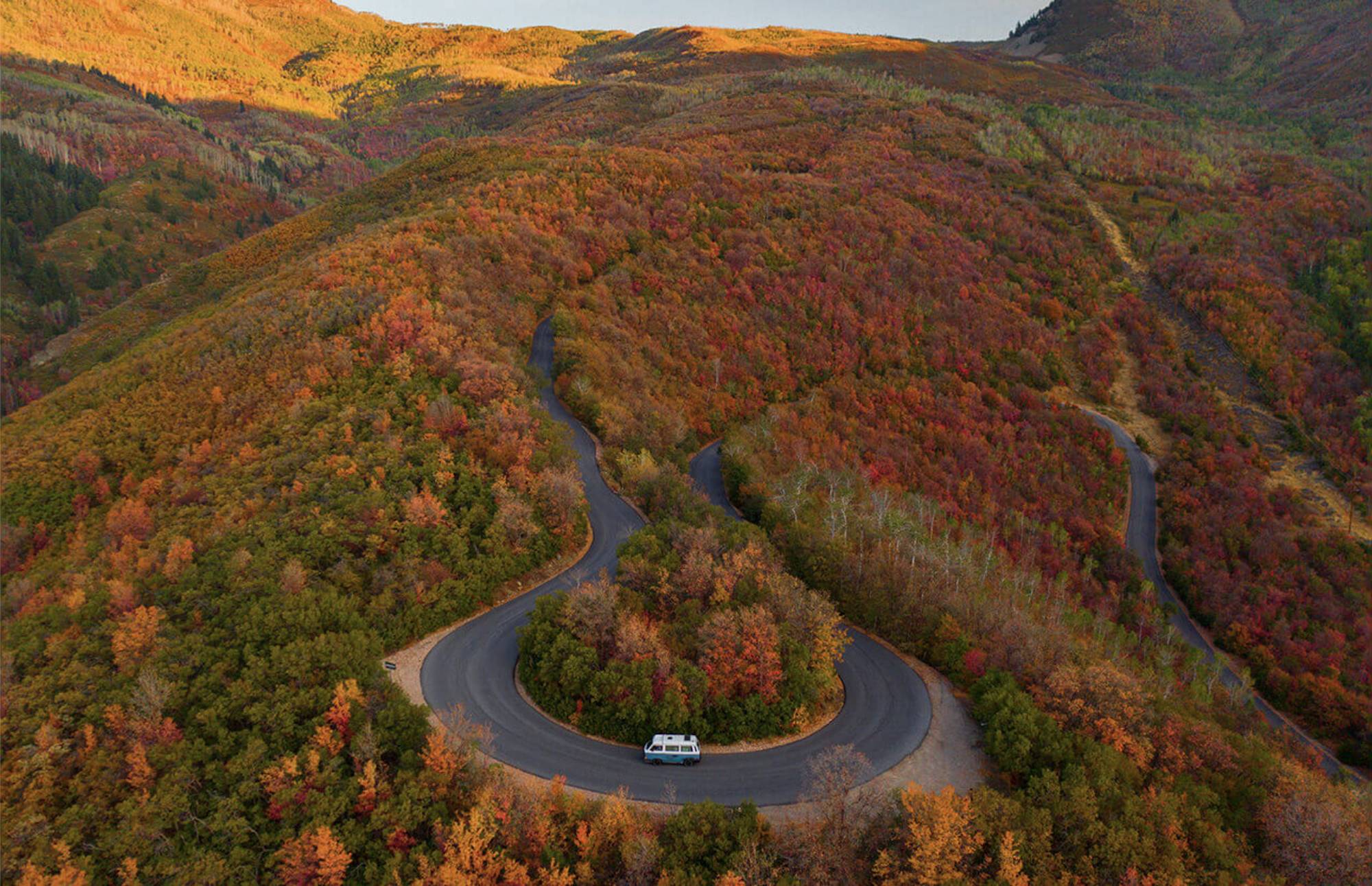 campervan driving up winding mountain road surrounded by fall foliage