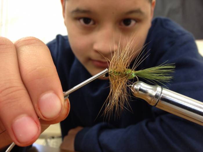 Young male kid learning how to tie a fly for fishing