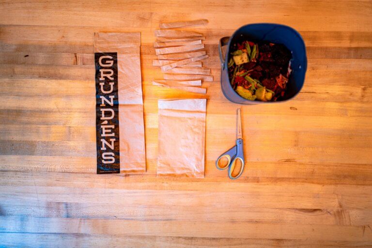 Compostable poly bags with the Grundéns’ logo next to a home compost bin on a wooden table