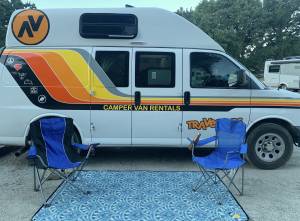 A rental campervan with outdoor blanket and camp chairs outdoors