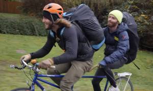 two men with duffel backpacks on a tandem bike
