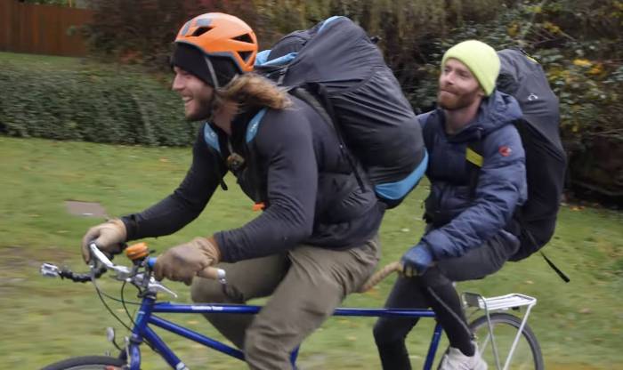 two men with duffel backpacks on a tandem bike