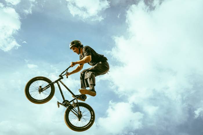 BMX biker riding Mongoose bike up in blue sky surrounded by clouds