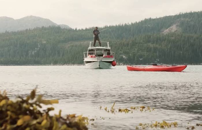 man fishing from boat with red kayak in foreground