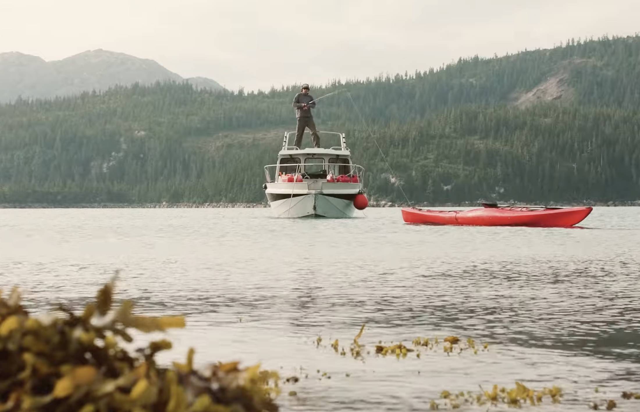 man fishing from boat with red kayak in foreground