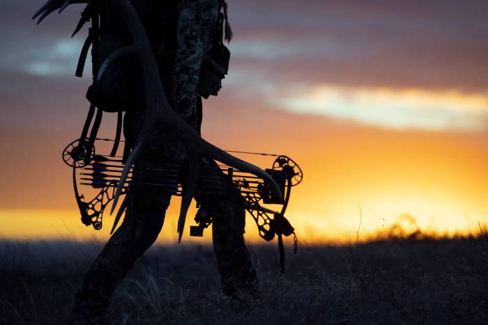 woman holding mathews bow walking into sunset