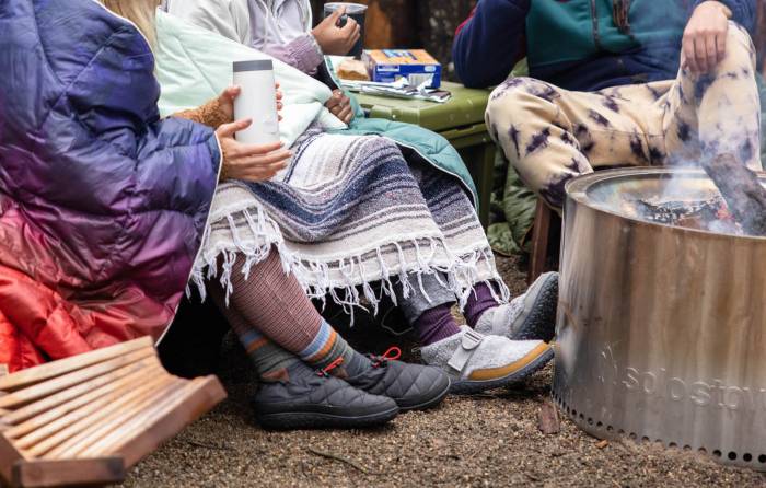 three people wearing Chaco's Ramble puff and fleece Ramble puff shoes around a Solo Stove fire pit