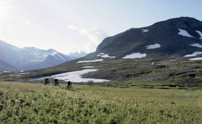 three FOX MTB riders going uphill in grassy trail in front of Canadian mountain range