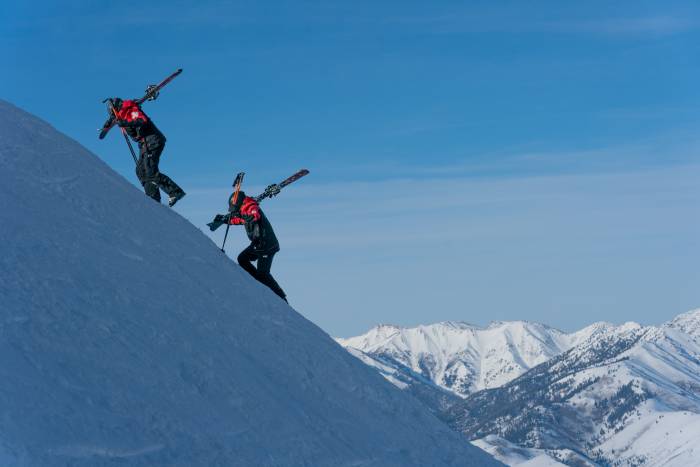 two ski patrollers climbing up a steep slope with their skis