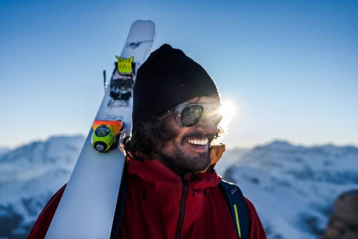 skier in red shell and beanie with Faction Agent Skis over should in the Dolomites