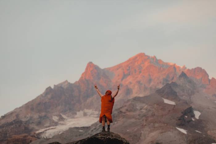 hiker in a sleeping bag with footbox unzipped somewhere along the Pacific Crest Trail with a mountain in pink hues in the background