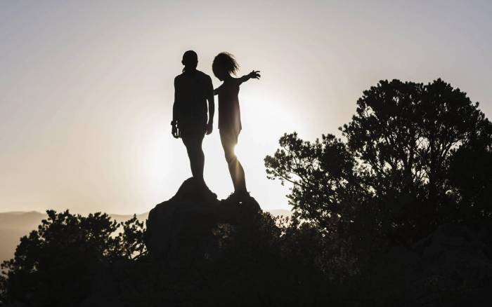 silhouettes of two runners standing a top a rock with the sun setting behind them