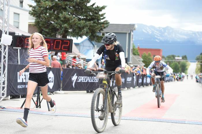 Verde PR founder Kristin Carpenter cycling towards the Leadville 100 Race finish with her daughter Bella running beside her