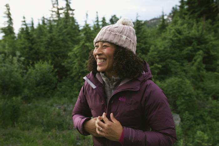 Black woman in a purple pink jacket and pom beanie hiking outdoors