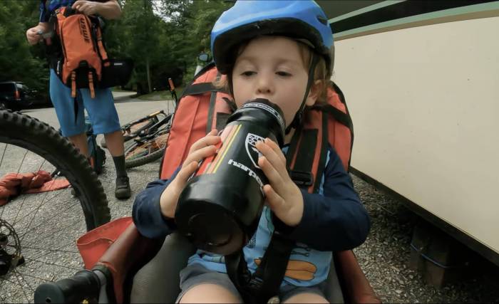 three year old toddler in bike carrier drinking out of water bottle