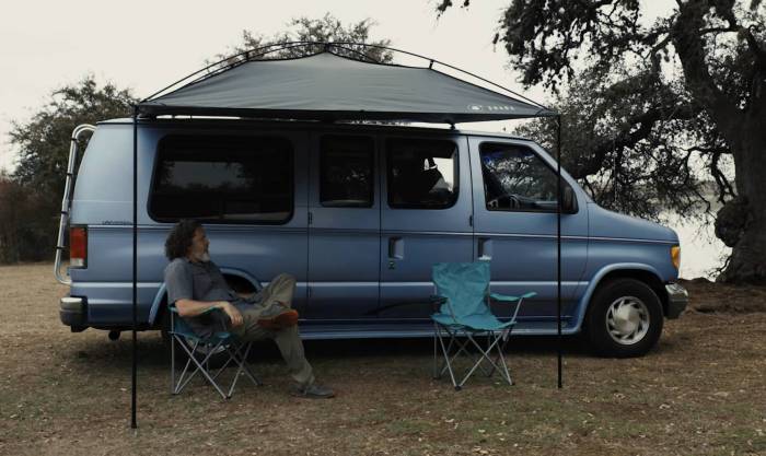 man with shoulder-length hair resting in a chair under a Moon Fab shade attached to his campervan