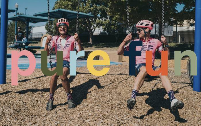 pro cyclists lachlan morton and alex howes in EF Pro pink kits playing on a swingset with an overlay of text that reads "pure fun"