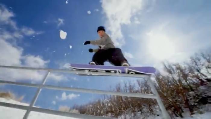 A female snowboarder sliding on a rail on a sunny day