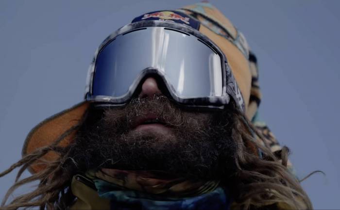 a bearded snowboarder john jackson wearing goggles looking out onto a ski line