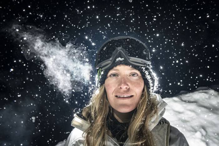 Jamie Anderson snowboarder standing in a winter jacket in goggles against a dark snowy backdrop